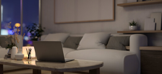 A laptop computer on a coffee table in a modern, cosy apartment living room at night.
