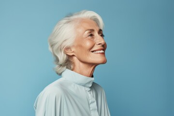 Cheerful senior woman looking away and smiling while standing against blue background
