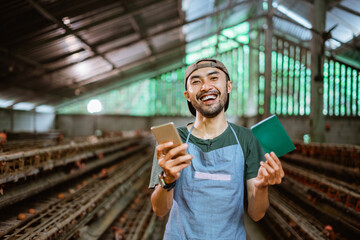 Happy Asian entrepreneurs work with smartphones and bankbooks on chicken farms