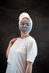 Young woman with a white towel applying cosmetic black mask of sea clay or mud isolated on black