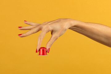 Crop woman showing coffee capsule over yellow background