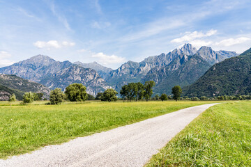 Mountain range in the Italian alps near lake Como on a sunny summer day with meadow and dirt road...