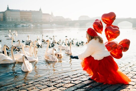 Woman with heart balloons on the river bank with swans in Prague