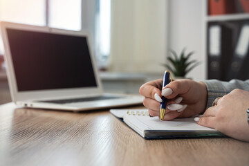Fototapeta premium close up female hand making note on notepad with laptop, work at office or job freelance at home