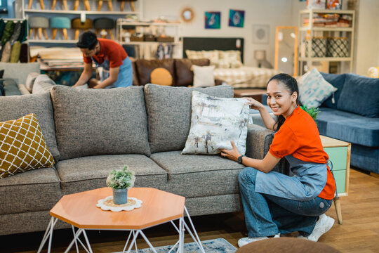 smiling female shop assistant squatting while arranging sofa cushions at a furniture store