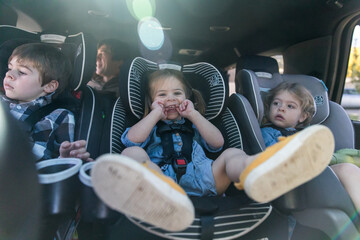 Three siblings strapped into carseats being silly