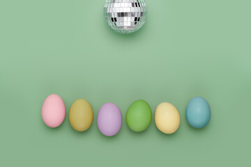Row of different colored eggs under mirror disco ball party on fun green background. Copy space simple pastel rustic background for traditional Easter holiday card