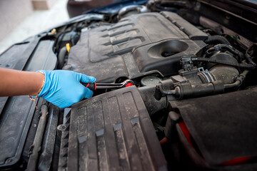 car mechanic repairs a car engine near a car with an open hood.