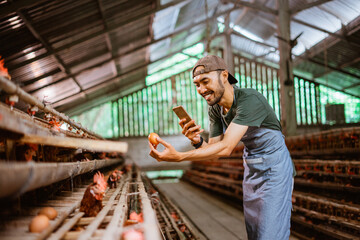 Young male entrepreneur taking a photo of an egg using a phone at a chicken farm
