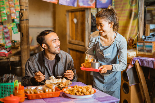 Asian female stall seller carrying a tray serving drinks to a male customer at a stall