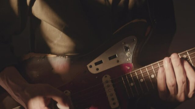 Tilt up shot of dimmed yellow rays of projector light shining on Caucasian male guitarist standing in dark room and playing electric guitar