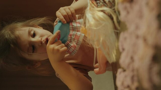 Little girl sitting at the table in the house dressing a doll, while playing alone
