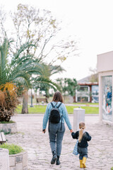Fototapeta na wymiar Mother and a little girl walk holding hands along a park alley. Back view
