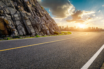 Asphalt highway road and mountain with city skyline at sunset