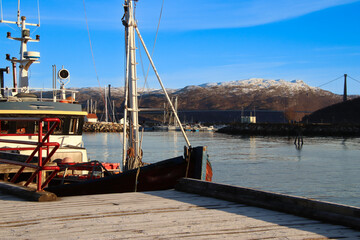 small harbor with a fishing boat in Norway with mountains in the background