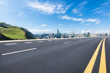 Asphalt road and green mountain with city skyline landscape under blue sky. high angle view.