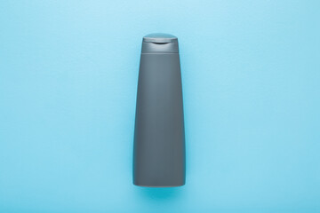 Gray plastic shampoo or shower gel bottle on light blue table background. Pastel color. Care about clean and soft body skin. Male beauty product. Closeup. Empty place for text or logo. Top down view.