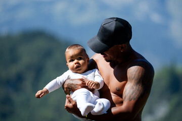 Close up portrait of afro american father kissing multiracial Biracial baby. Father hug Biracial child oudoor. Father with Biracial baby on nature. Hathers hand carrying Biracial baby.