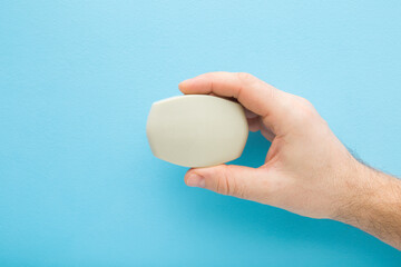 Young adult man hand fingers holding natural soap on light blue table background. Pastel color....