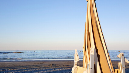 beautiful sunrise with sun reflection on cesenatio riccione rimini beach with open umbrellas - obrazy, fototapety, plakaty