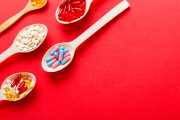 Vitamin capsules in a spoon on a colored background. Pills served as a healthy meal. Red soft gel vitamin supplement capsules on spoon