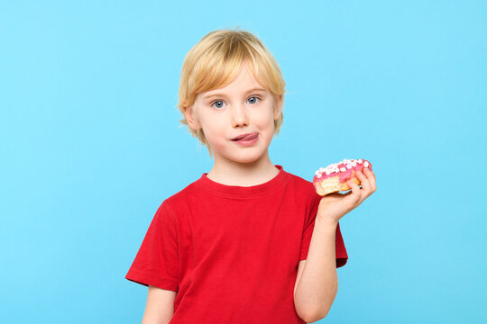 Cute little boy with blond hair and freckles having fun with glazed donuts, sticking tongue out. Children and sugary junk food concept. Boy holding colorful donuts.