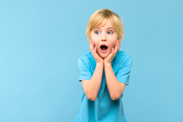 Wow! Portrait of a shocked cute little boy with blond hair on pastel blue background. Surprised preschooler studio shot, looking to side. - obrazy, fototapety, plakaty
