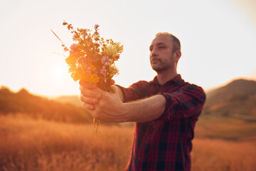 Man picking and holding field flowers in nature.
