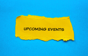 Upcoming events lettering on ripped yellow paper piece with blue background. Top view, copy space...