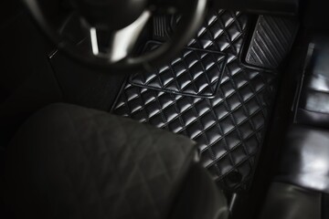 The driver’s side of a luxury car with a leather floor mat. The interior is modern and elegant,...