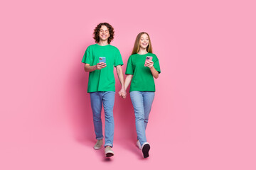 Full length body photo of two youth best friends steps with smartphones addicted playing mobile games isolated on pink color background