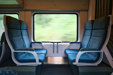 Empty blue seats in passenger train with blurred foliage outside window.