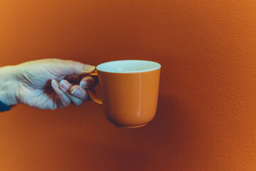 Orange coffee mug mockup for design demonstration. Cup mock up in female hands on orange wall...