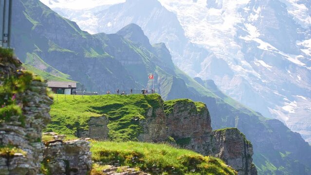 Swiss flag waving, tourists admire peak of Jungfrau mountain on Mannlichen viewpoint, Bernese Oberland in Switzerland