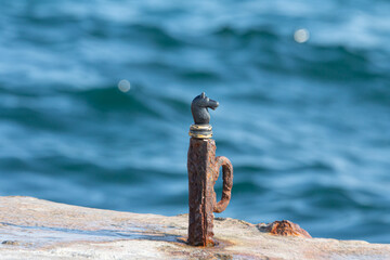 A black chess horse stands on a rusty metal pin against the background of the sea
