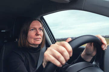 Caucasian female holding car steering wheel and driving through countryside landscape