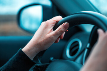 Female hands on car steering wheel. Woman driver traveling along the road through countryside...