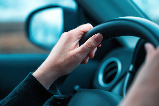 Female hands on car steering wheel. Woman driver traveling along the road through countryside landscape. Road trip concept for endless possibilities