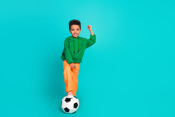 Full length photo of cute cheerful small boy raise hands fist yes goal victory empty space isolated on cyan color background