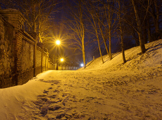 Park wieczorową porą, śnieg, latarnie oraz stary mur. - obrazy, fototapety, plakaty