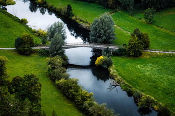 Fototapeta premium Brücke über einen Fluß. Wiese und Bäume, reflektionen im Wasser. Donau Flußweg. Ufer mit Büsche und Bäumen.