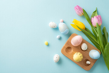 Fototapeta na wymiar Spring joy vibes! Cheerful Easter top view scene with vibrant eggs in a wooden holder, and fresh tulips. Pastel blue backdrop adds charm. Perfect for text or advertisements