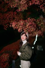 Asian woman in a chic jacket, experiencing the magic of Christmas in Japan's urban night. A festive...