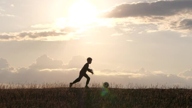 Silhouette of a child running on a hill and kicking a ball with his foot. The child dreams of becoming a soccer player, the boy is playing soccer. children's lifestyle, outdoor activities