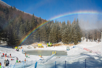 Family winter ski resort Il Lago della Ninfa. Monte Cimone, mountains in the northern Apennines, of Italy, Emilia-Romagna. Slope for children sleighing, snow tubing. Rainbow. People figures