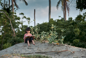 A cute little girl sits under a tree reading a book in the tropical forest