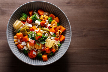 Autumn pasta salad with roasted pumpkin, broccoli, feta cheese on dark wooden background, fall...