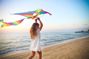 Little girl with flying kite on tropical beach at sunset