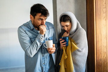 Portrait of a sick couple having a cold and flu. Wrapped in blanket, freezing and drinking hot drink