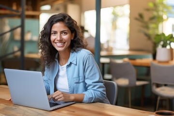 Fototapeta na wymiar Young smiling hispanic woman wearing casual denim shirt using laptop in a coffee shop